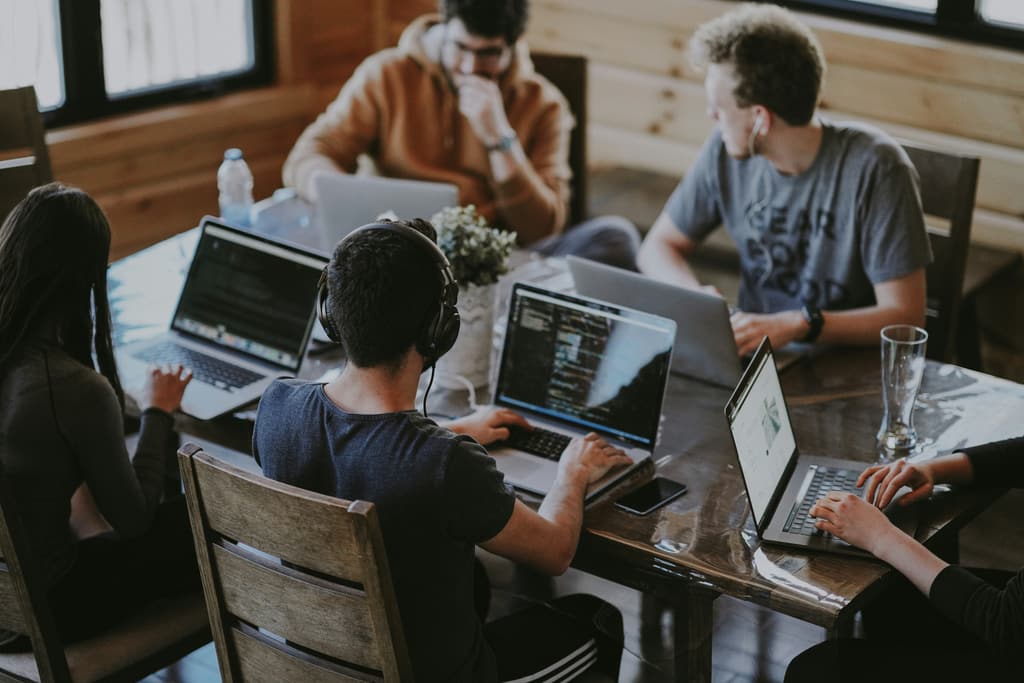 Several people working with laptops around a shared wooden table.